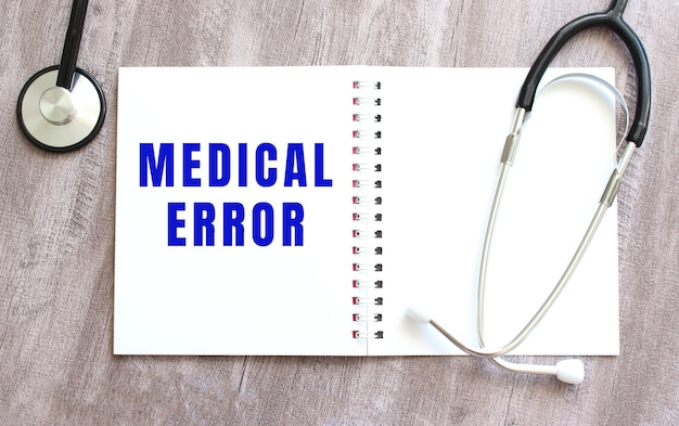 A white notebook with the words MEDICAL ERROR and a stethoscope on a gray wooden table. Medical concept