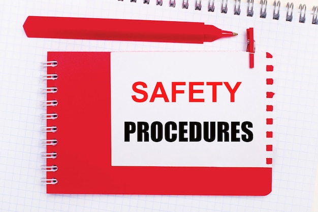 Photo on a white notepad a red pen a red notepad and a white sheet of paper with the text safety procedures