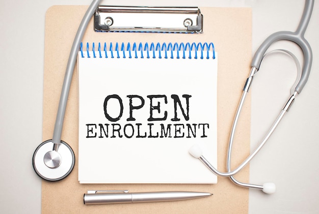 White notepad with the words open enrollment and a stethoscope on a blue background. Medical concept