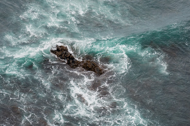 White ocean waves crashing over coastal sea rocks in summer.