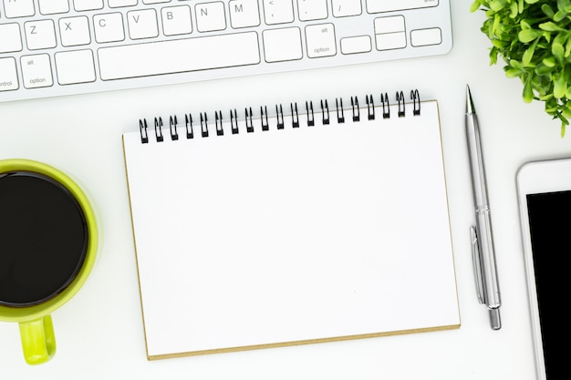 White office desk table with blank notebook page and supplies. Top view, flat lay.