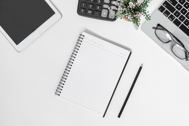 White office desk table with blank notebook, tablet, calculator, computer and other office supplies