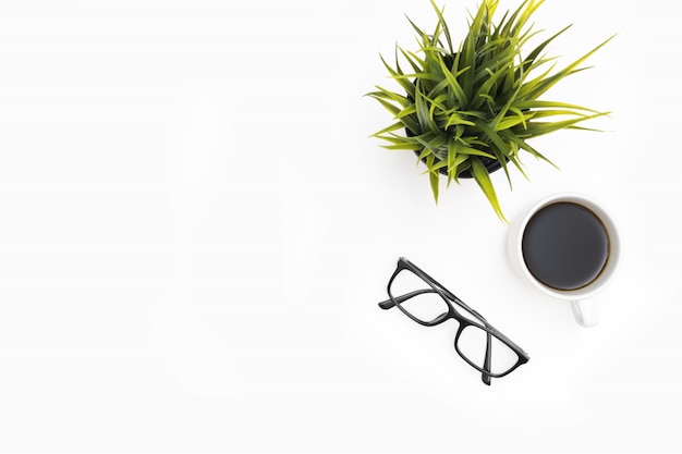 White office desk table with cup of coffee, eye glasses and a grass pot. 