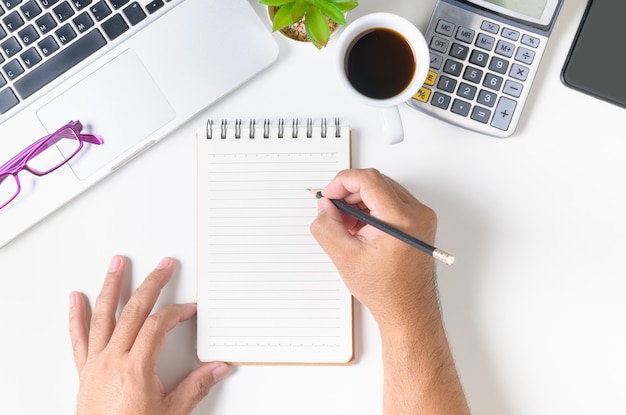 White office desk table with hand man writing something on blank notebook