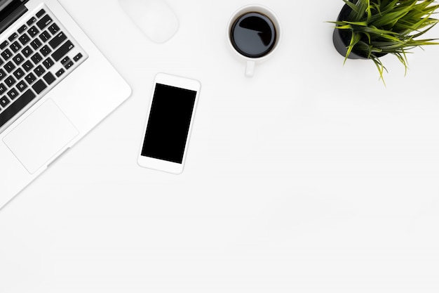 White office desk table with laptop computer, smartphone, cup of coffee and supplies. 