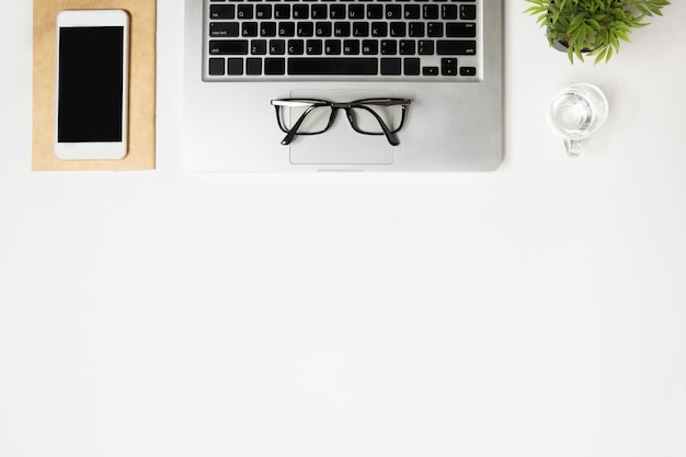 White office desk table with laptop computer, smartphone and supplies. Top view with copyspace, flat lay.