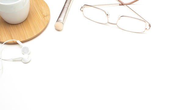 On a white office table, gold-framed glasses, a white cup on a wooden stand, headphones and a makeup brush. Women's business. Copy space