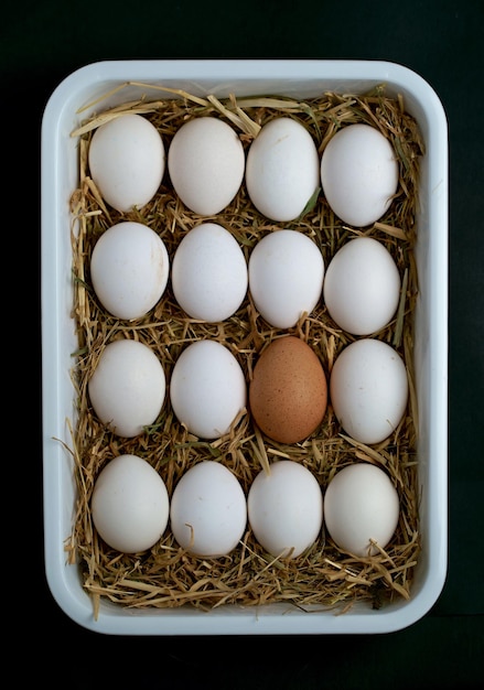 White and one brown raw farm chicken eggs lie on a black background