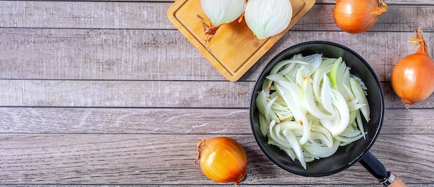 White onion slices in pan for cooking and fresh white onion on gray backgroundTop view