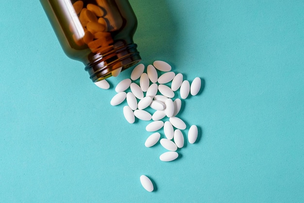 White oval medical pills pouring out of a medicine bottle on a blue background