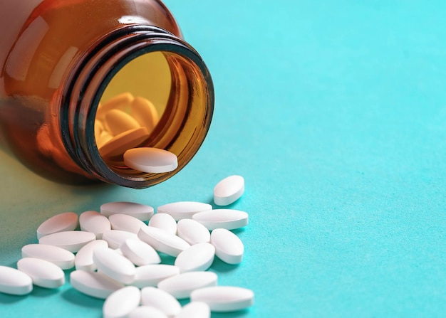 White oval medical pills pouring out of a medicine bottle on a blue background