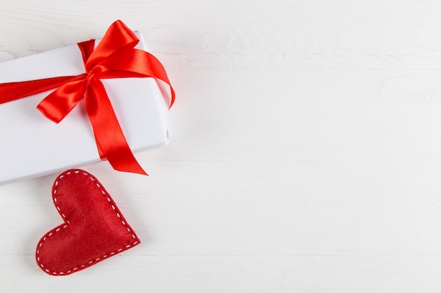 White packed gift with red ribbonnd handmade heart on the table.