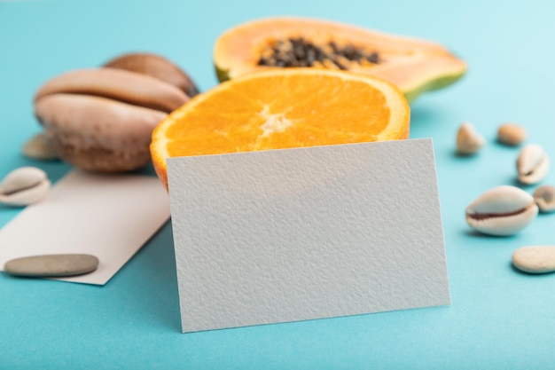 White paper business card with ripe cut papaya orange seashells on blue pastel pastel background Side view close up