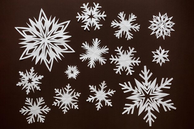 White paper snowflakes different shapes and sizes on brown cardboard background Top view