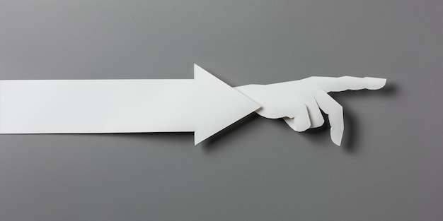 Photo white paper strip folded into shape of arrow with cut out hand pointing towards right gray bg