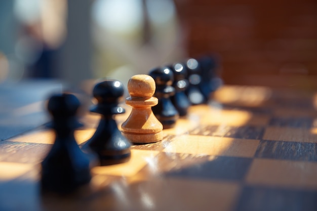 A white pawn between black chess pieces on an old chessboard