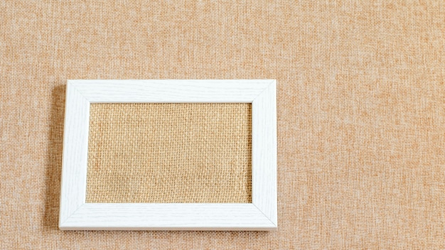 White pciture frame blank on the eco friendly textured burlap fabric. Mock up photo.