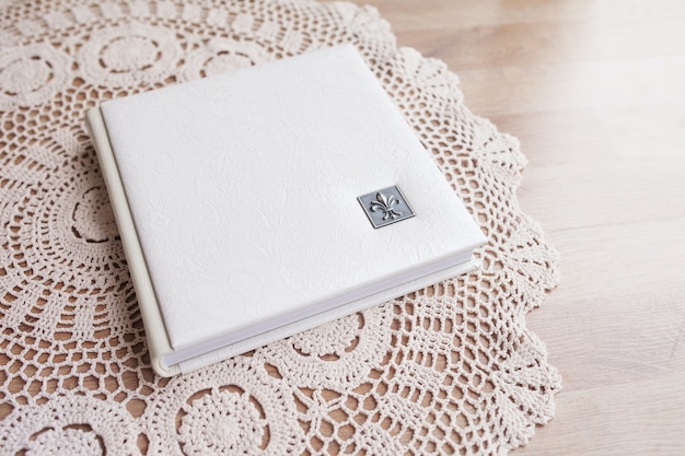 White photo book with leather cover. Stylish wedding photo album.  Family photoalbum on the white table . Beautiful notepad or photobook with elegant openwork embossing on a white table.