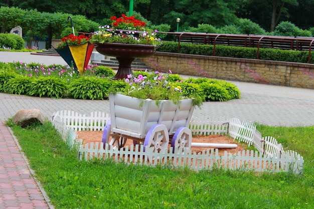 A white picket fence surrounds a garden with a wagon full of flowers.