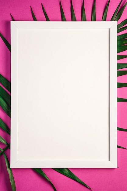 White picture frame with empty template on palm leaves, pink purple background 