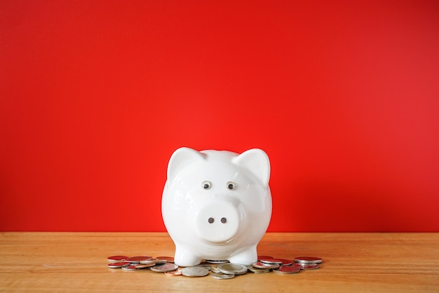 White Piggy bank and coin on wooden desk with red background