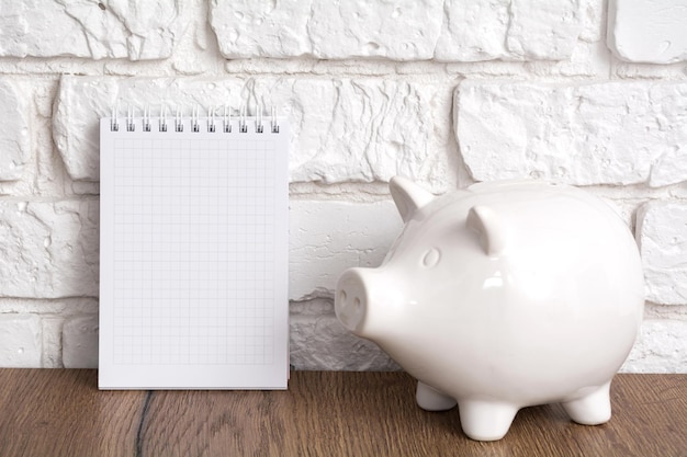 White piggy bank and notebook on a white brick background Saving concept