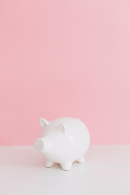 Photo white piggybank on white desk over the pink background