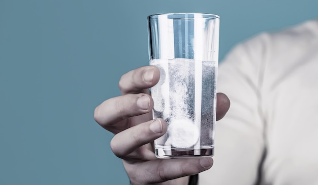 White pill and a glass of water in man hands Glass of water tablet Glass with efervescent tablet in water with bubbles