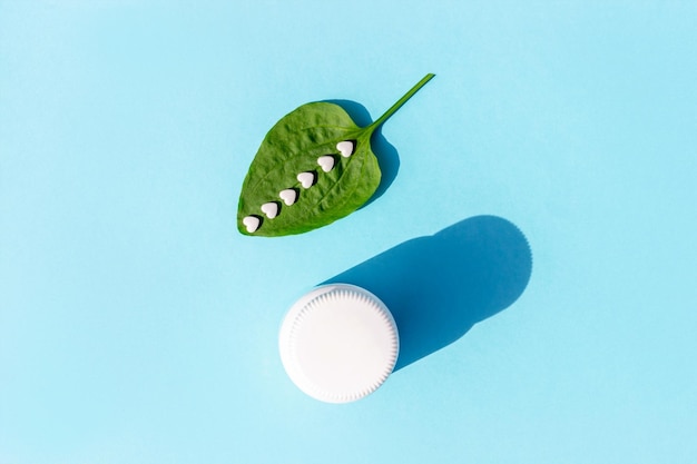 White pills on green plantain leaf and of bottle on blue background Homeopathy naturopathy nutraceuticals and healthcare concept Top view Flat lay