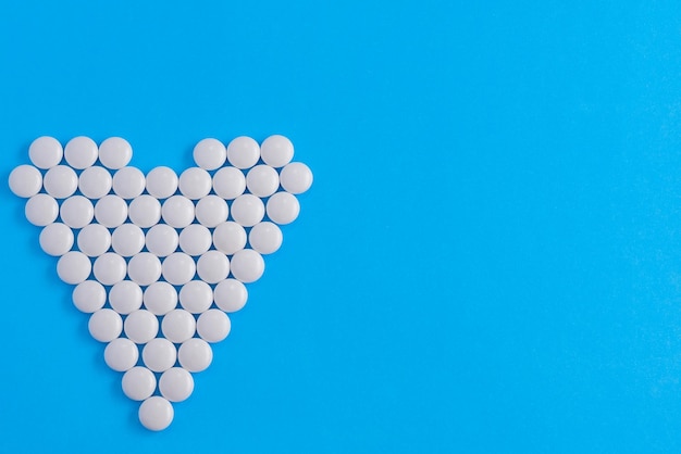 White pills laid out in the shape of a heart on a blue background