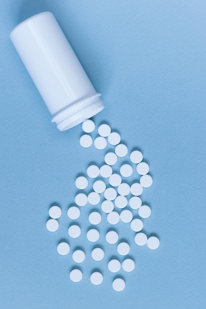 White pills scattered from the container on the blue background