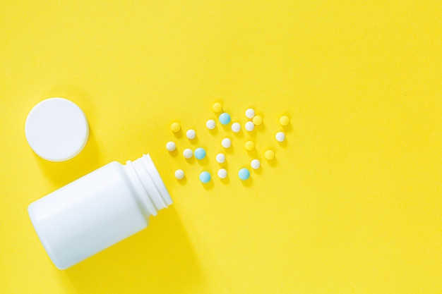 White pills and white bottle with copy space on yellow background Healthy and Medicine concept