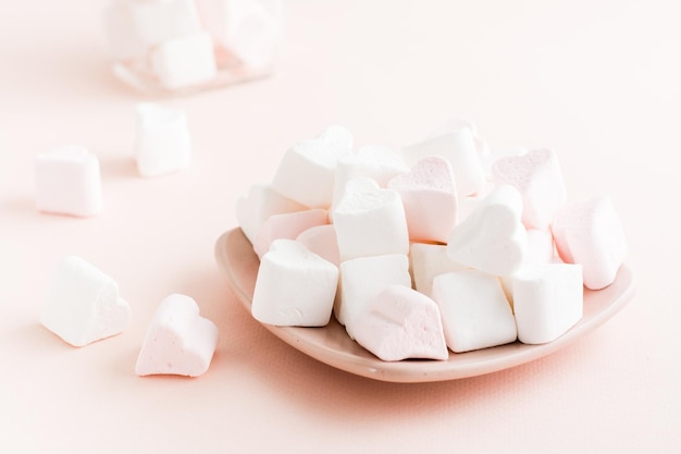 White and pink heartshaped marshmallows on a saucer on a pink background