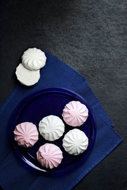 White and pink marshmallow on blue plate on black background. Flat lay, top view, copy space