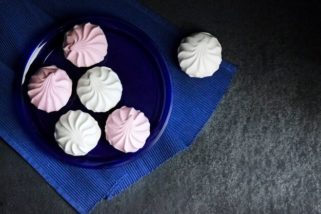 White and pink marshmallow on blue plate on black background. Flat lay, top view, copy space