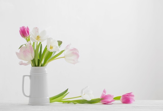 White and pink tulips in jug on white background