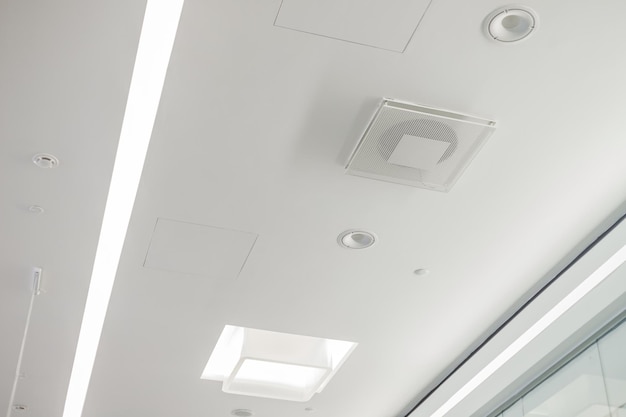 White plasterboard ceiling in administrative and public building with ventilation, lamps and speakers.