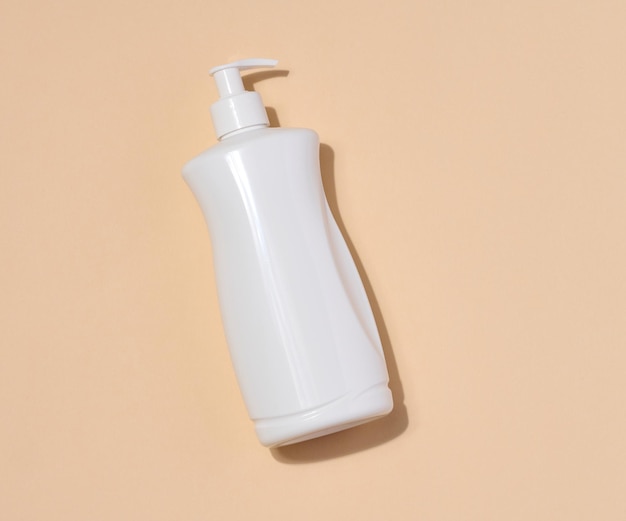 White plastic container with a pump for liquid products on a beige background Container for cosmetics soap cream