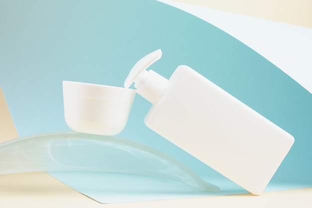 White plastic cream bottle with dispenser and cream jar on plastic podium on light blue background