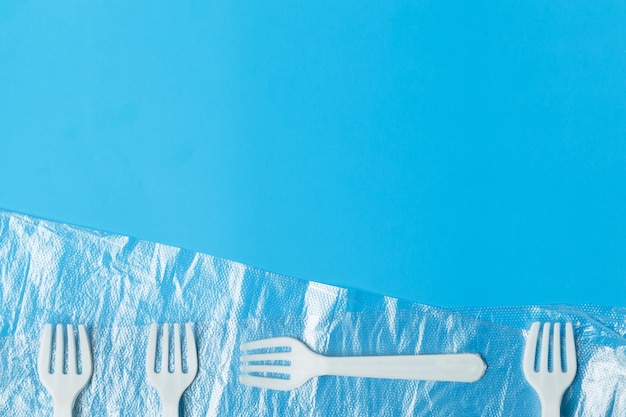 White plastic forks and transparent plastic bag on a blue background The global problem of environmental pollution Copy space flat lay minimalism