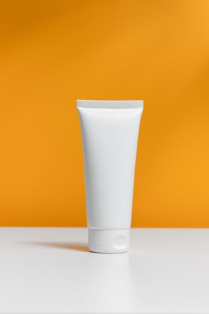 A white plastic jar of cream stands on an orange isolated background empty space for your design