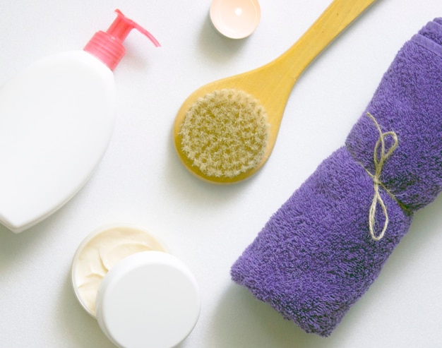 White plastic jars with creams, purple towel, candle, brush for dry massage. The concept of Spa, body care. Top view