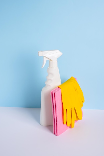 White plastic spray bottle and yellow rubber protective glove on a rag on blue background The conce