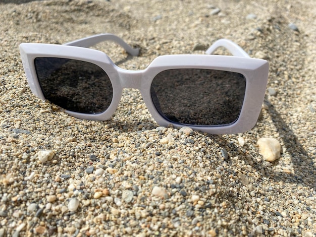 White plastic sunglasses for women on the yellow sand of a beach in a warm eastern tropical