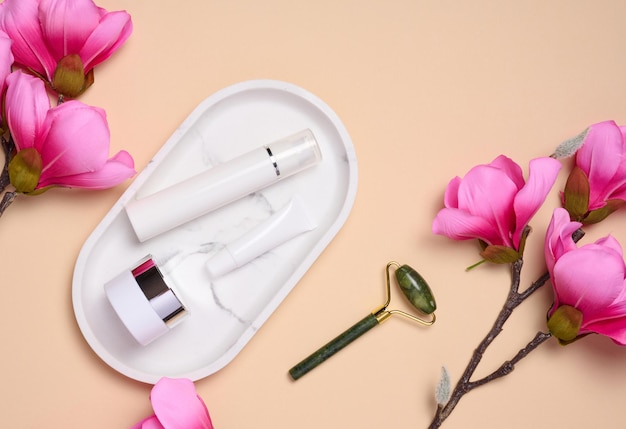 White plastic tub jar on a marble stand and a bouquet of pink magnolia top view