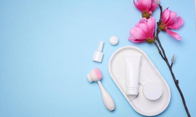 White plastic tubes and jars of cream and a massage brush for facial cleansing on a blue background items for cosmetic procedures