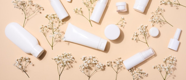 White plastic tubes jars and gypsophila branches on a beige background containers for cosmetic creams and gels advertising and brand promotion top view