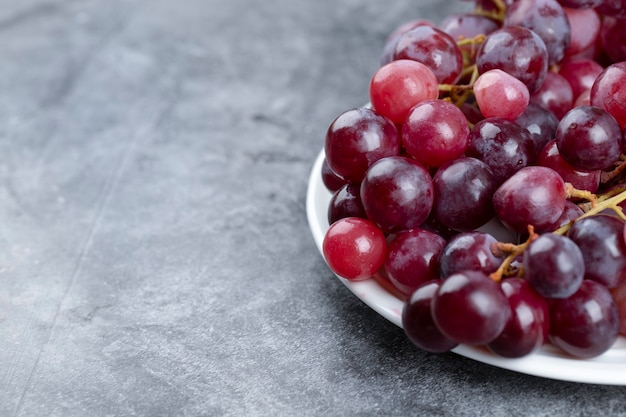 White plate of fresh red grapes on stone background. 