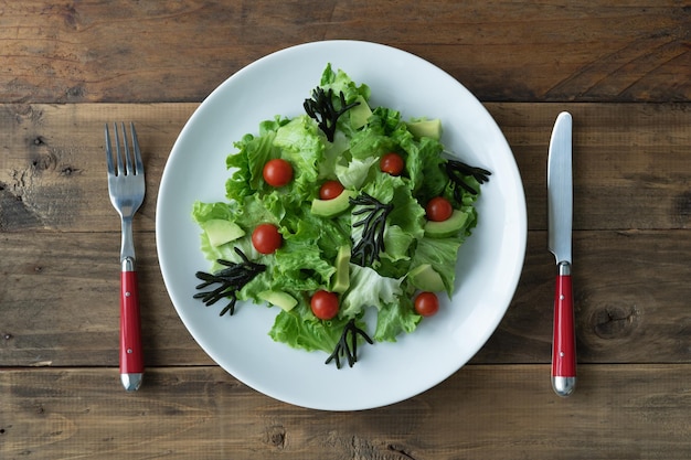 White plate of mixed salad with seaweed tomatoes lettuce and avocado Wood background Copy space