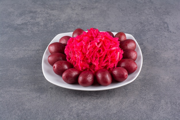 White plate of pickled plums and cabbage on stone table.